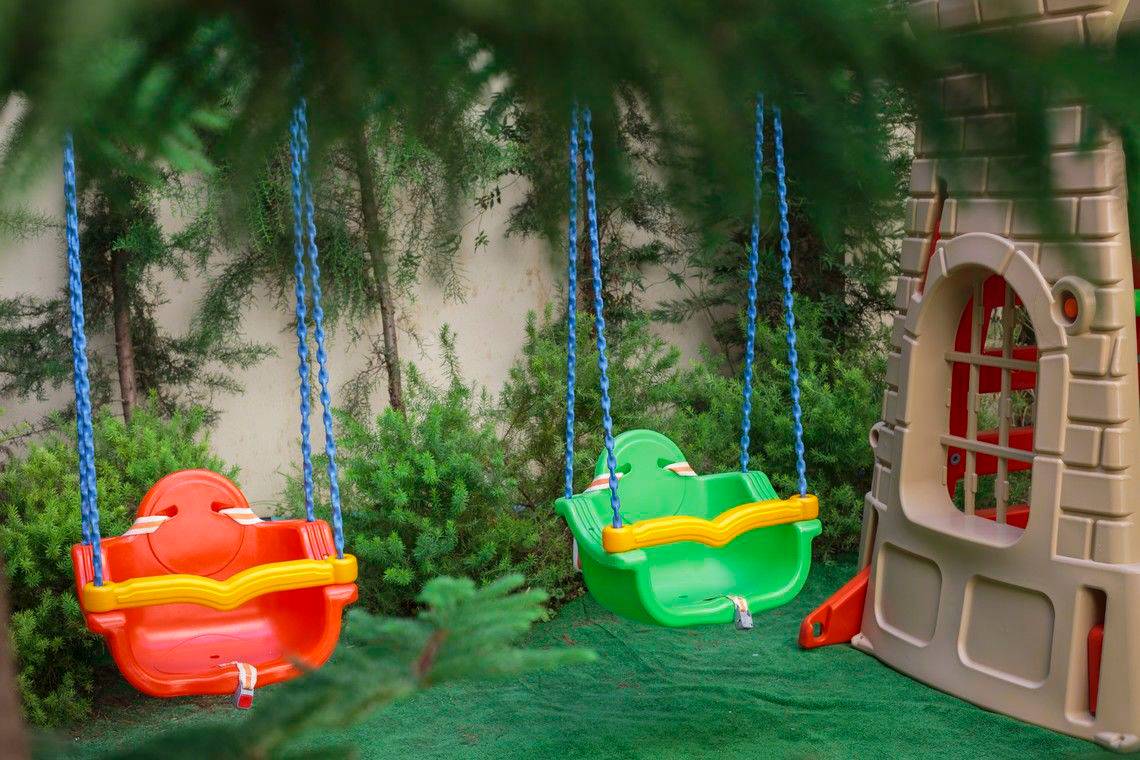 Zwei bunte Schaukeln und ein Spielhaus im Garten des Well Palace Side Hotels.