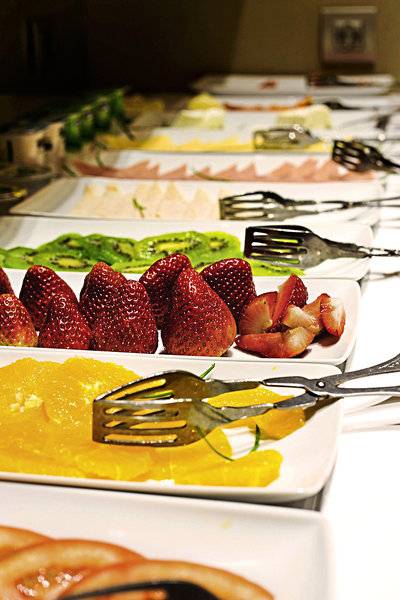 Buffet mit verschiedenen Obstsalaten und Früchten wie Erdbeeren, Kiwis und Orangen.