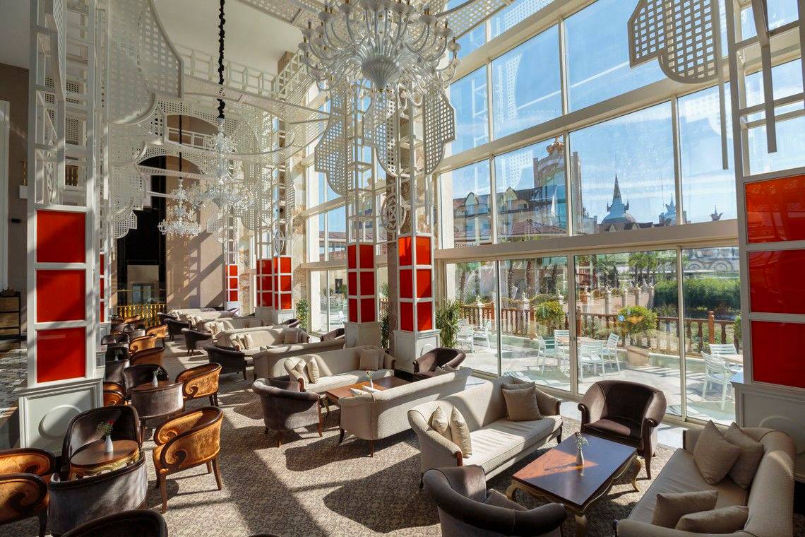 Lobby des Well Palace Side Hotels mit weißen Möbeln, roten Akzenten und großen Fenstern.