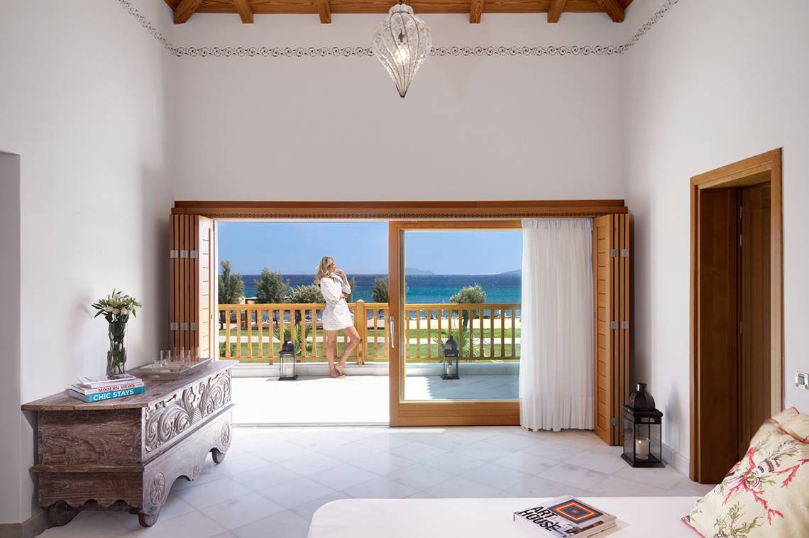 Innenansicht eines Zimmers im Mitsis Blue Domes Resort & Spa mit Blick auf eine Terrasse und das Meer.