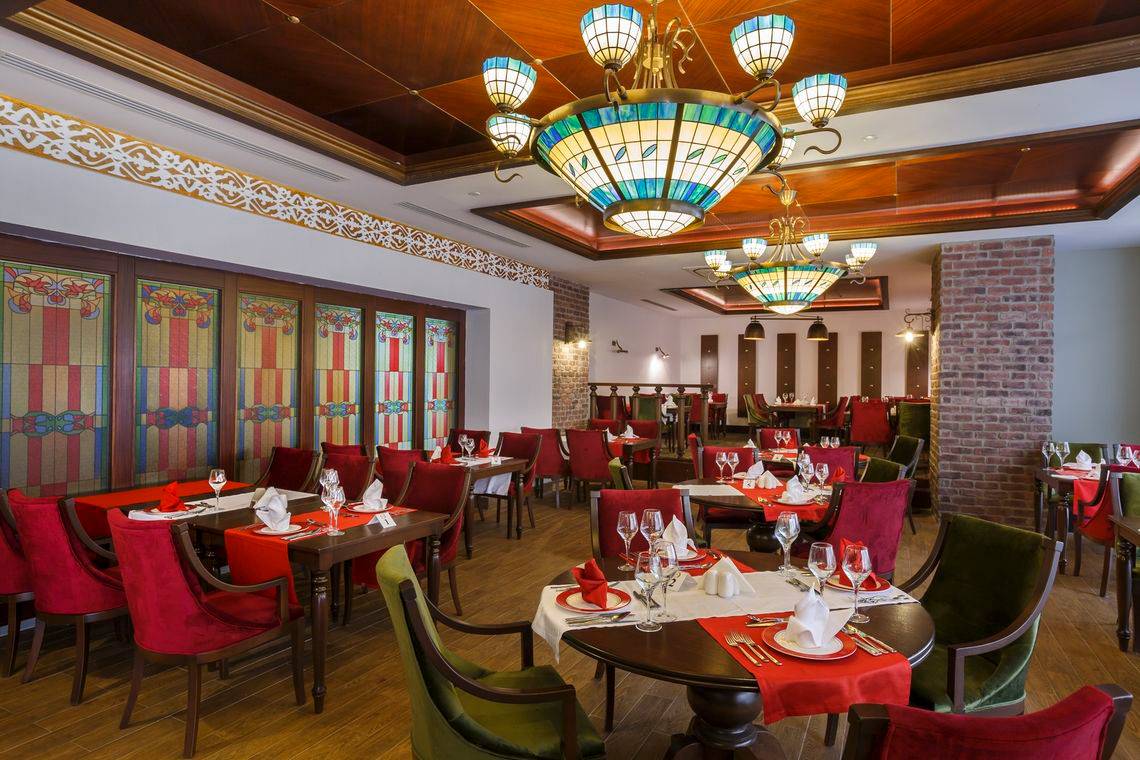 Innenansicht des Restaurants im Well Palace Side Hotel mit kunstvollen Kronleuchtern und farbigen Glasfenstern.