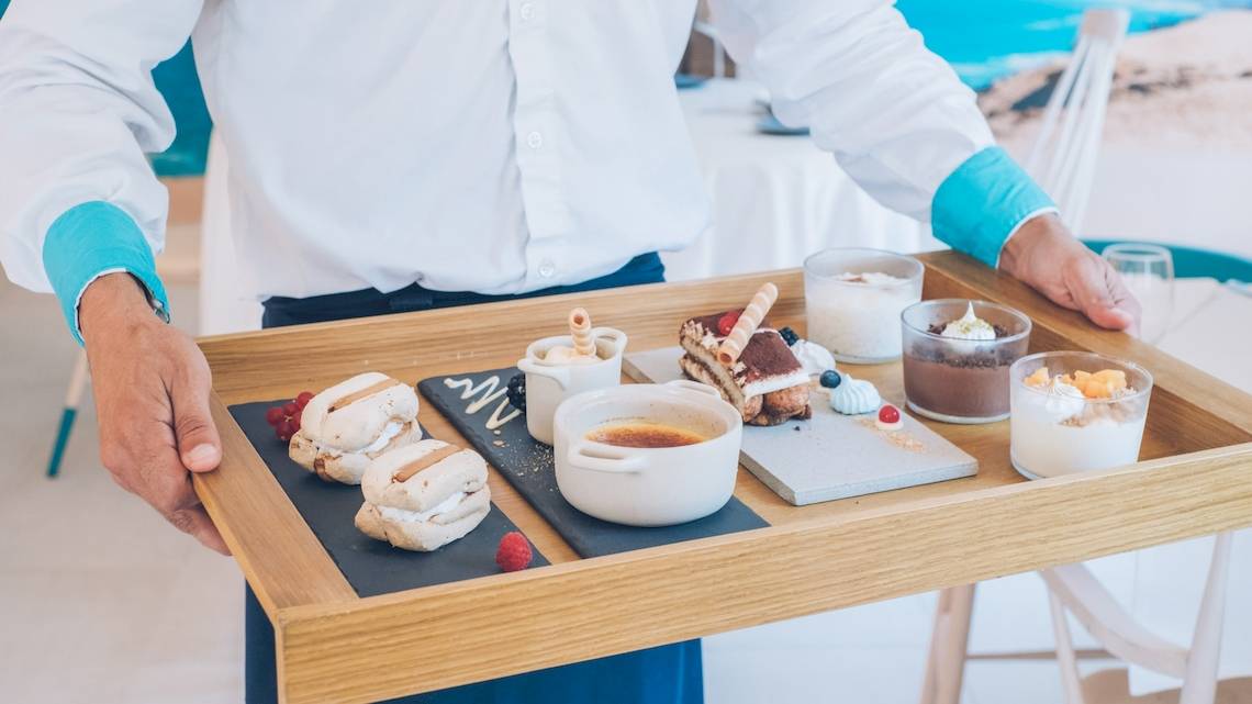 Ein Kellner serviert eine Holztablett mit verschiedenen Desserts und Speisen im Iberostar Selection Playa de Palma Hotel.