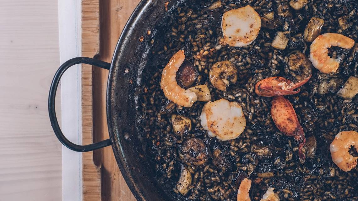 Nahaufnahme einer Paella in einer Pfanne mit Garnelen, Muscheln und Tintenfisch auf einem Holzbrett
