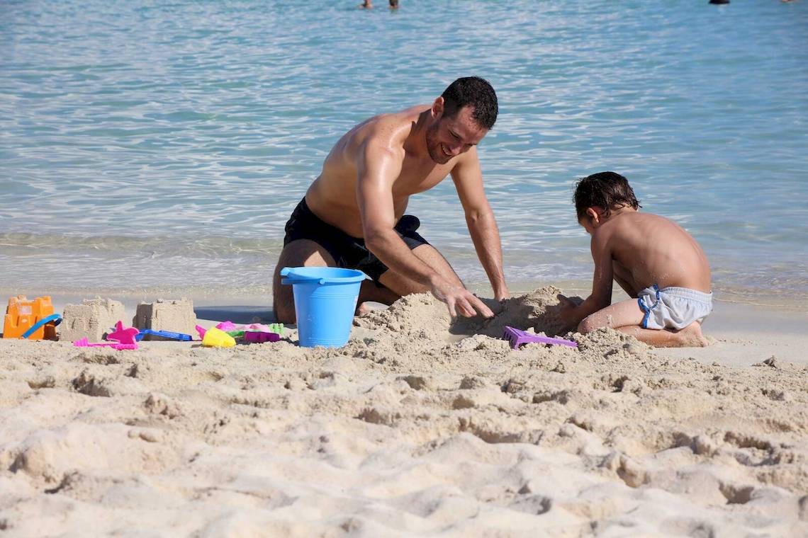Vater und Sohn bauen Sandburg am Strand des Bahia Principe Grand Tulum.
