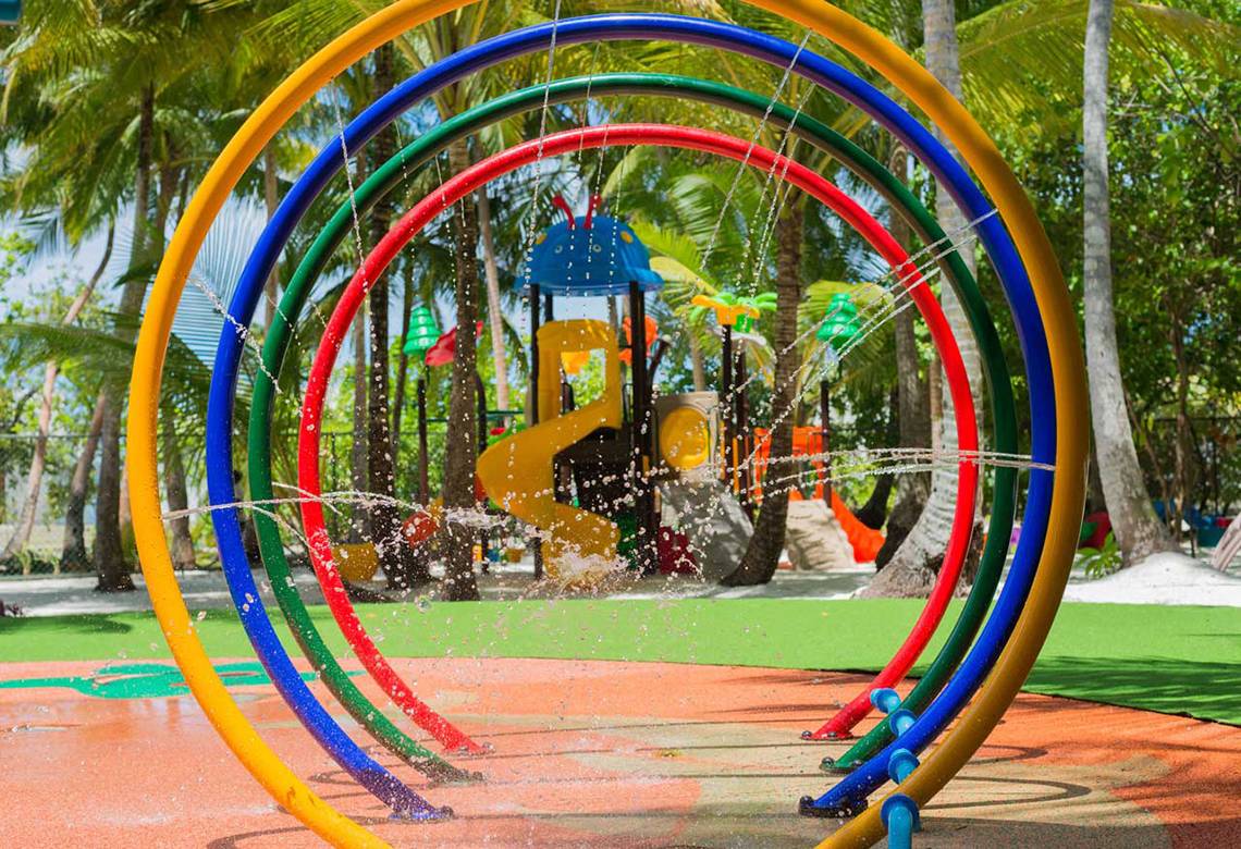 Spielplatz im Dhigali Maldives mit bunten Wasserspielkreisen und Palmen im Hintergrund.