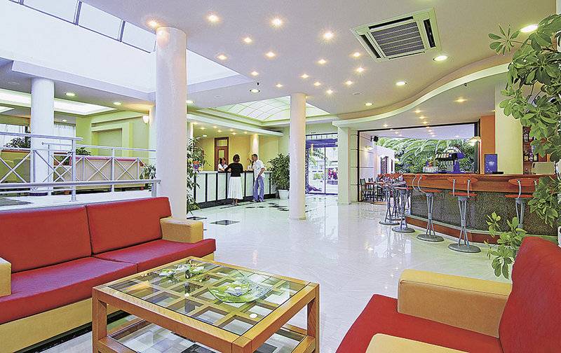 Empfangsbereich des Eva Bay Hotels mit roten Sofas, Bar und Empfangstresen.