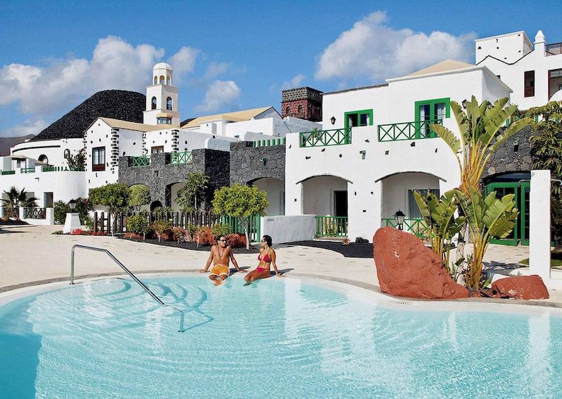 Zwei Gaeste sitzen im Pool des LIVVO Volcan Lanzarote Hotels vor weissen Gebaeuden.
