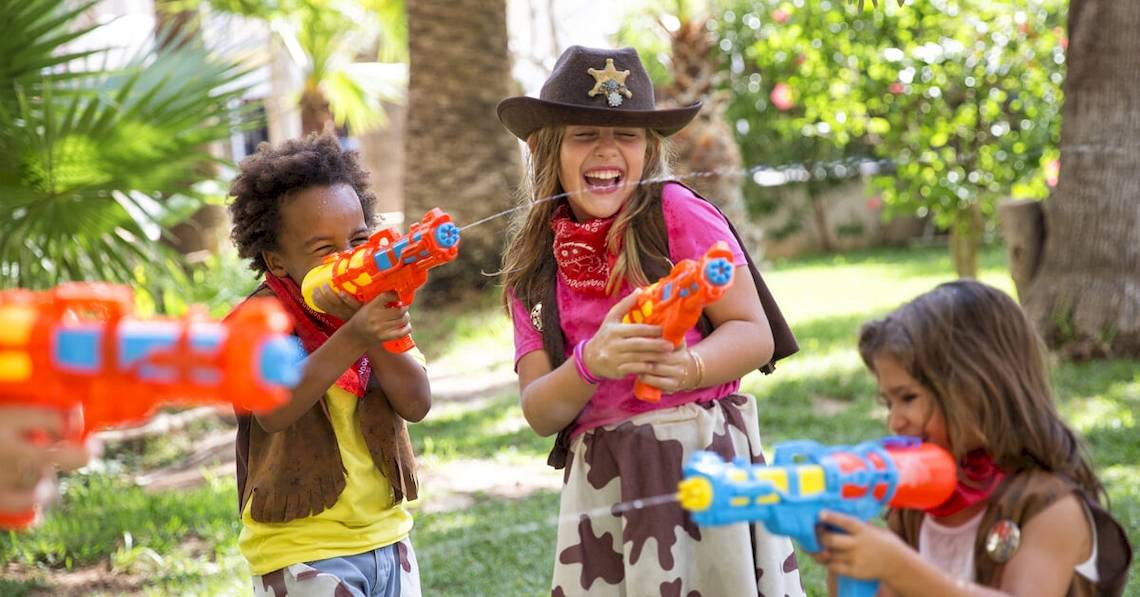 Drei Kinder spielen mit Wasserpistolen im Garten des Sol Principe Hotels.