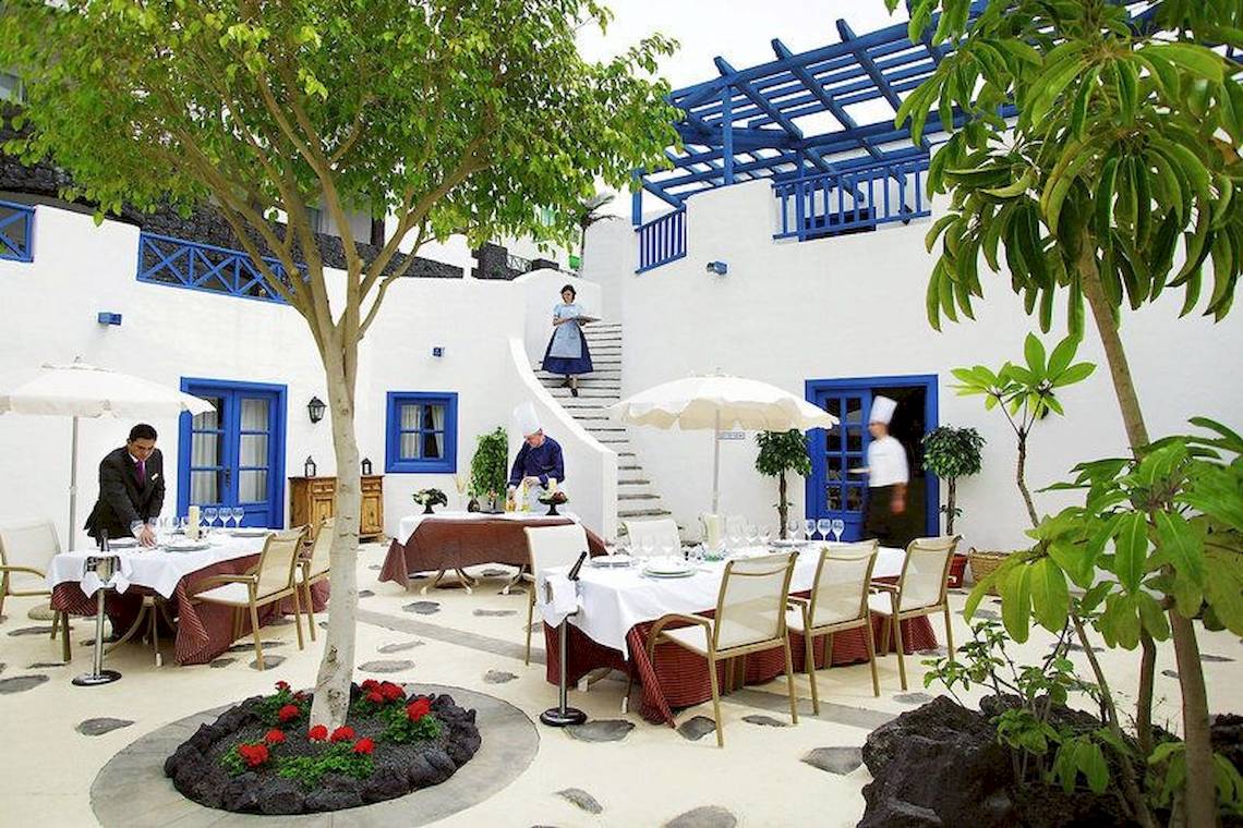 Außenbereich des LIVVO Volcan Lanzarote Hotels mit Tischen unter Umbrellas und Gästen.