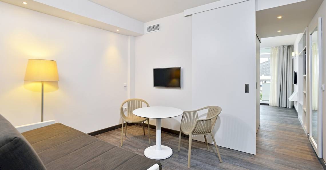 Ein modernes Hotelzimmer von Sol Principe mit weißem Tisch, Stühlen und Fernseher an der Wand.