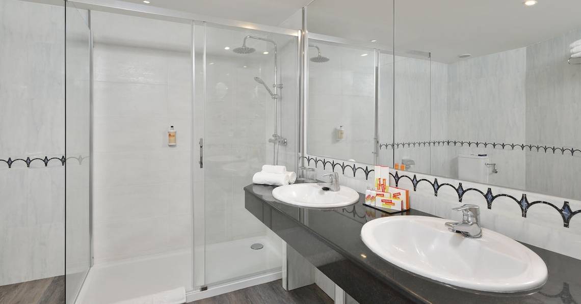 Das Badezimmer im Sol Principe Hotel mit einer Dusche, zwei Waschbecken und einem Spiegel.