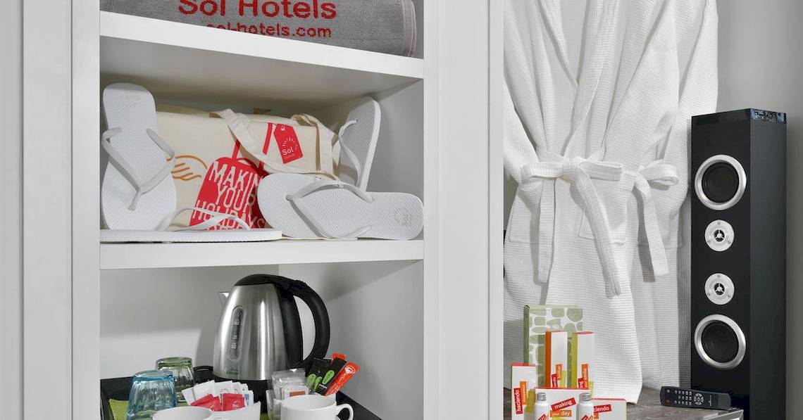 Ein Hotelzimmer des Sol Principe mit einem Schrank, Flip-Flops, einem Wasserkocher und weiteren Gegenständen.