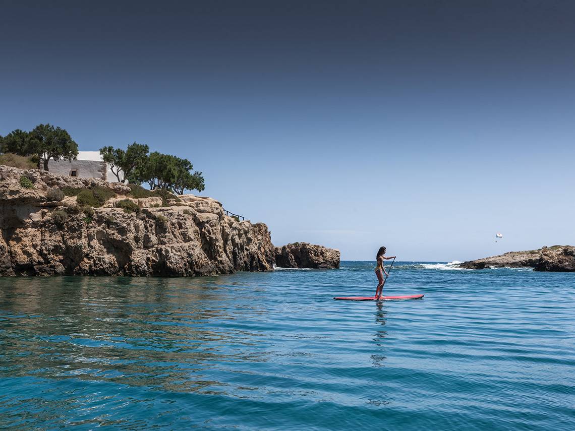 Frau auf einem SUP-Board im Wasser vor einem Felskliff