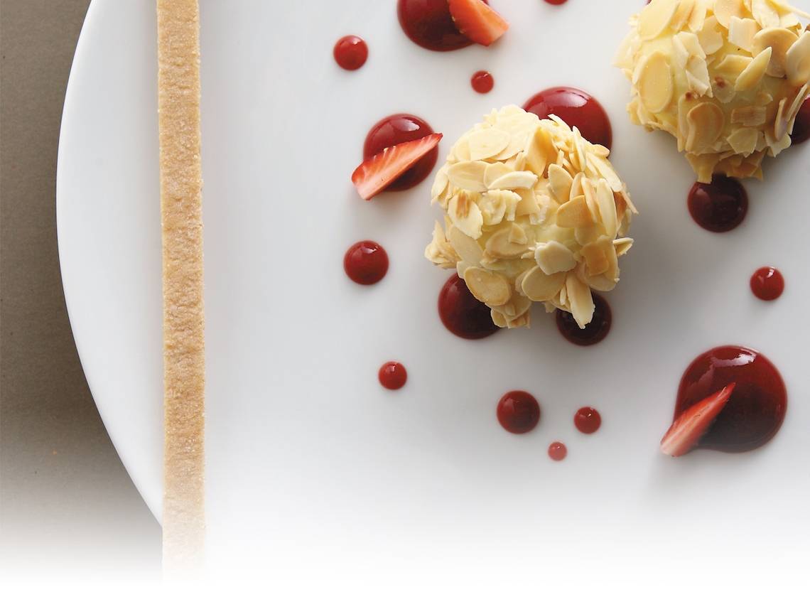 Mandel-Schoko-Kugel auf weissem Teller mit Erdbeeren und roter Glasur