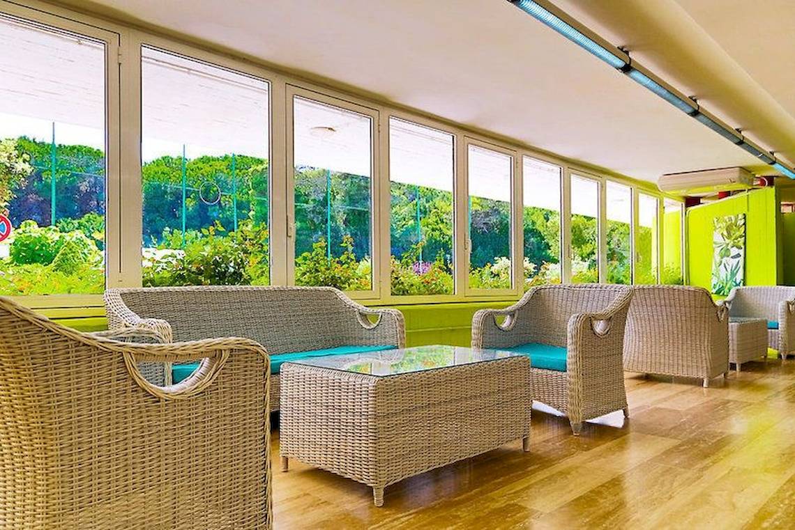 Loungebereich des VOI Alimini Resorts mit Rattanmöbeln und großen Fenstern.