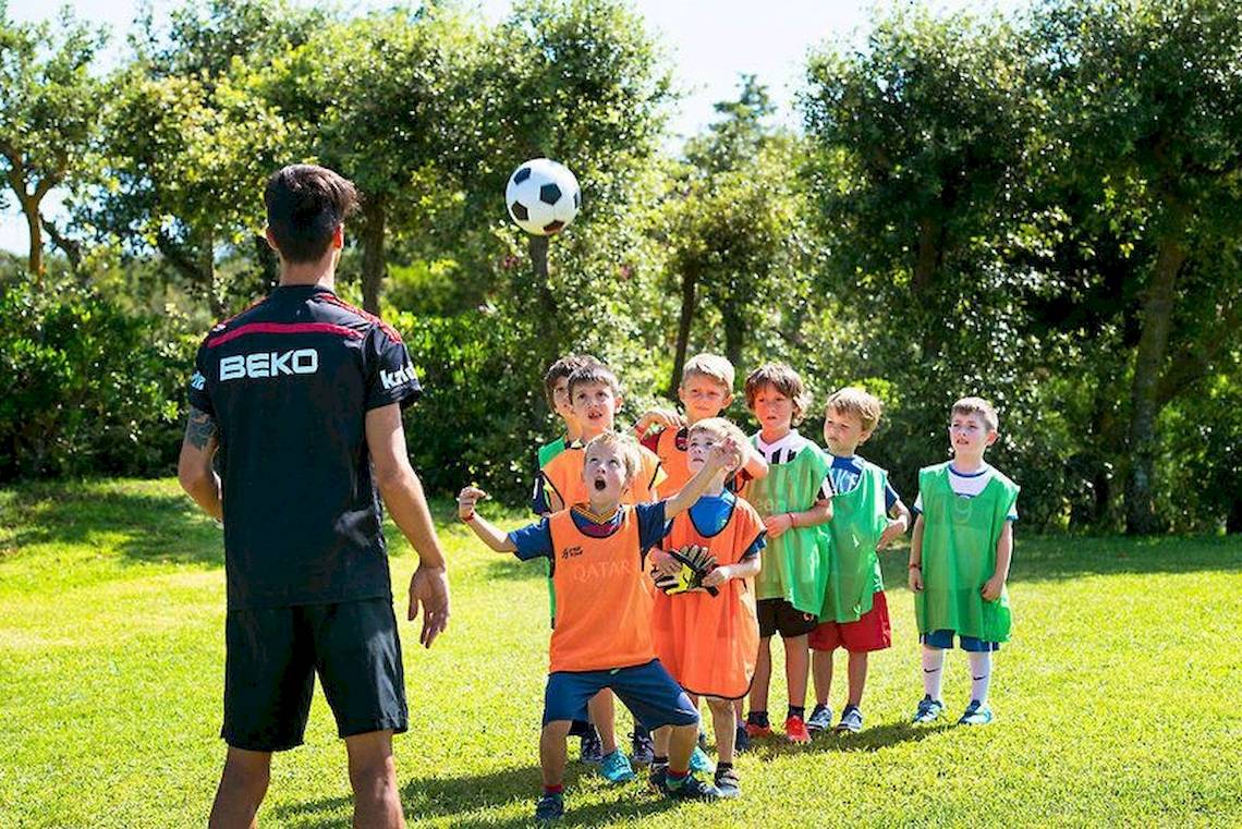 Kinder spielen Fußball im Freien mit einem Trainer auf dem VOI Alimini Resort