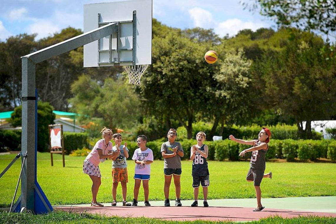 Kinder spielen Basketball am VOI Alimini Resort während eine Frau den Ball wirft.