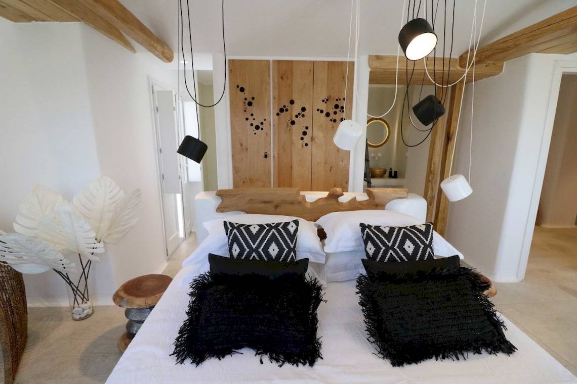 Schlafzimmer im Alkyoni Beach Hotel mit weißem Bett, schwarzen Kissen und Holzelementen.