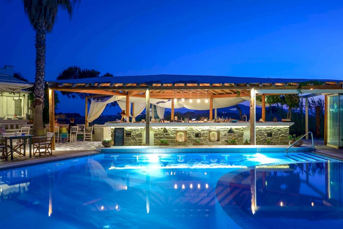 Der Pool des Alkyoni Beach Hotels bei Nacht mit Beleuchtung und Barbereich.