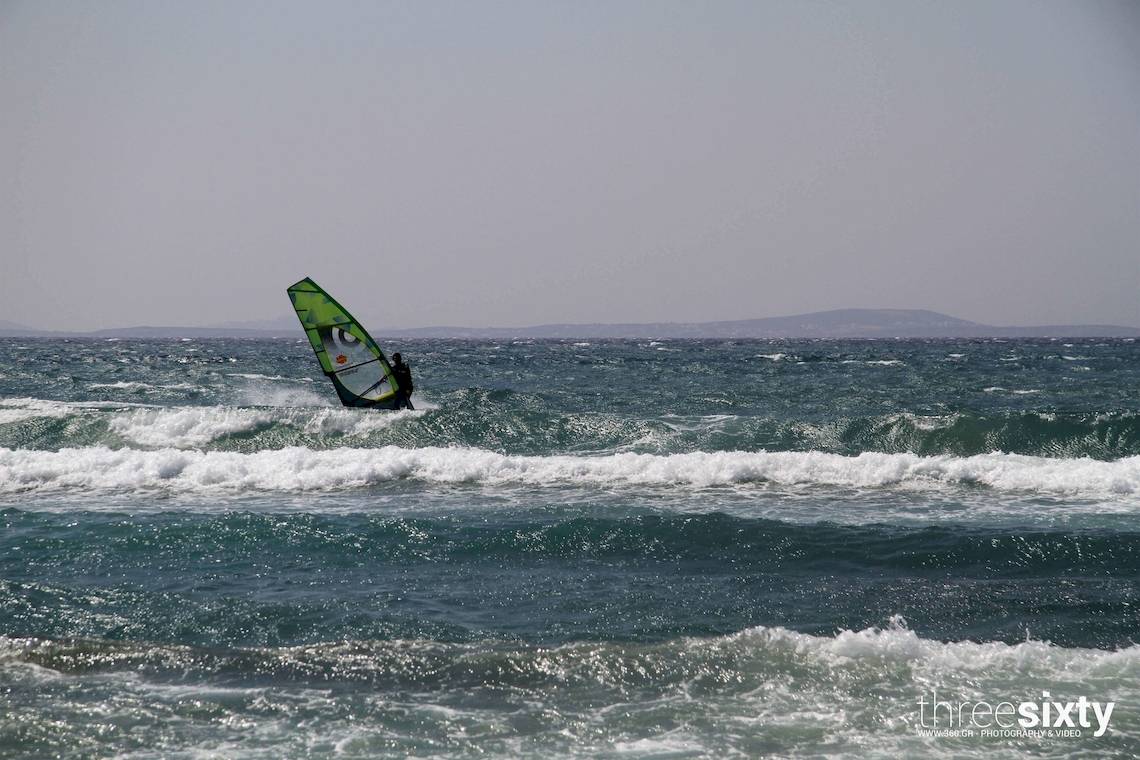 Eine Person windsurft in stürmischem Ozean mit hohen Wellen.