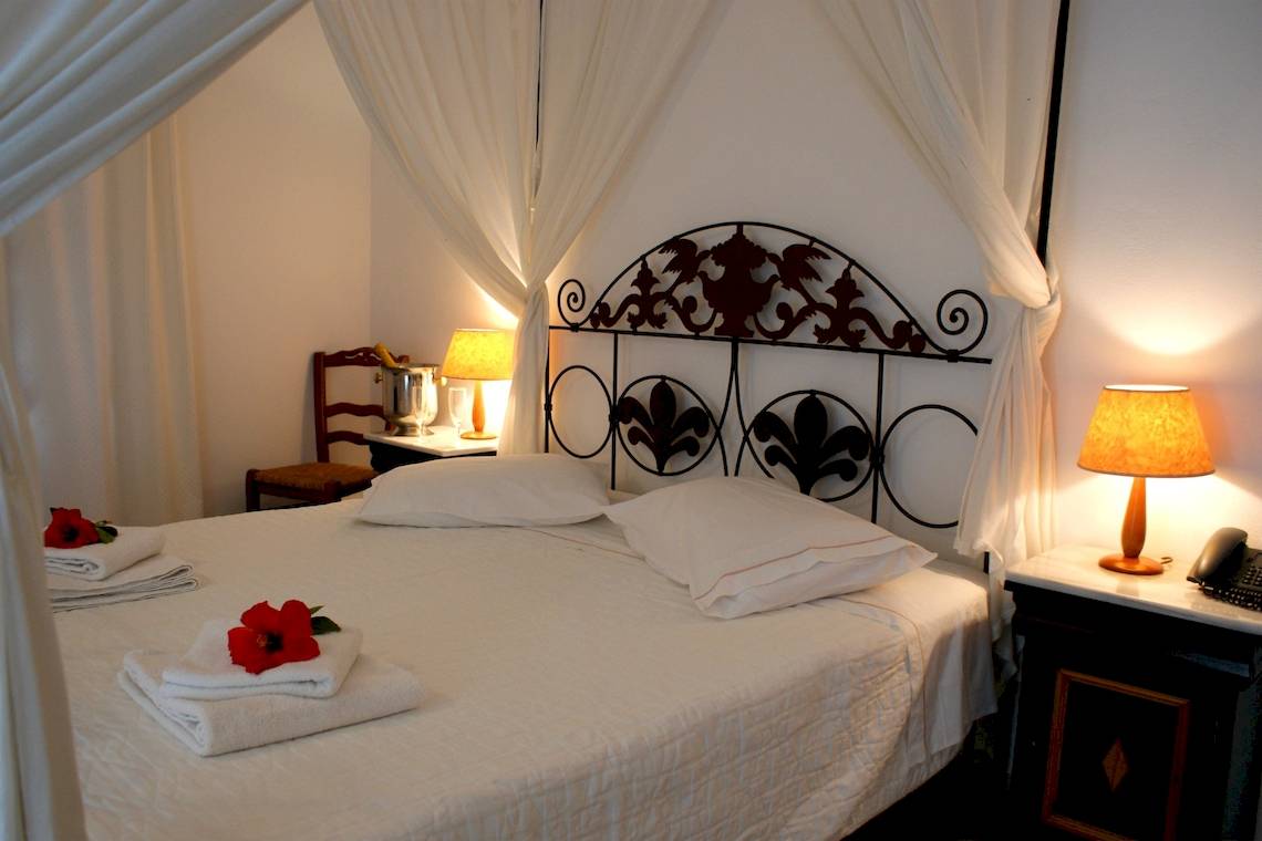 Ein Bett mit weißen Laken und Kissen im Alkyoni Beach Hotel, neben einem Nachttisch mit Telefon und Lampe.