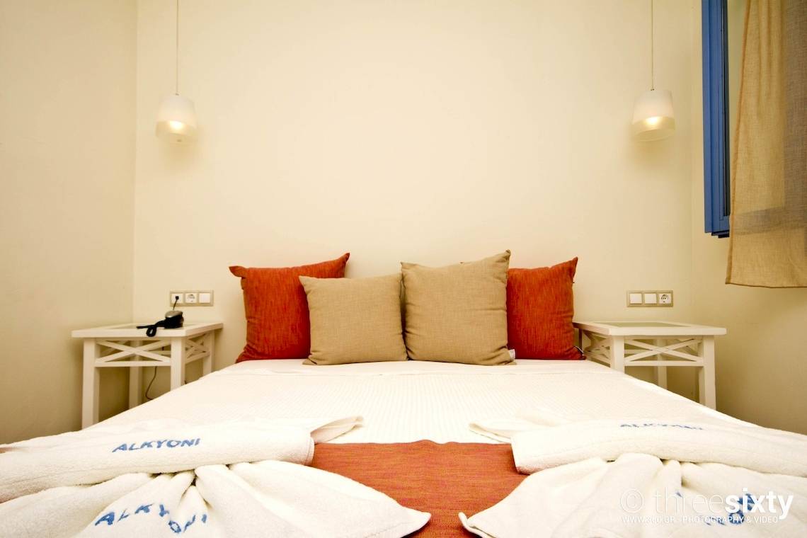 Ein Schlafzimmer im Alkyoni Beach Hotel mit zwei Nachttischen und zwei Lampen an der Wand.