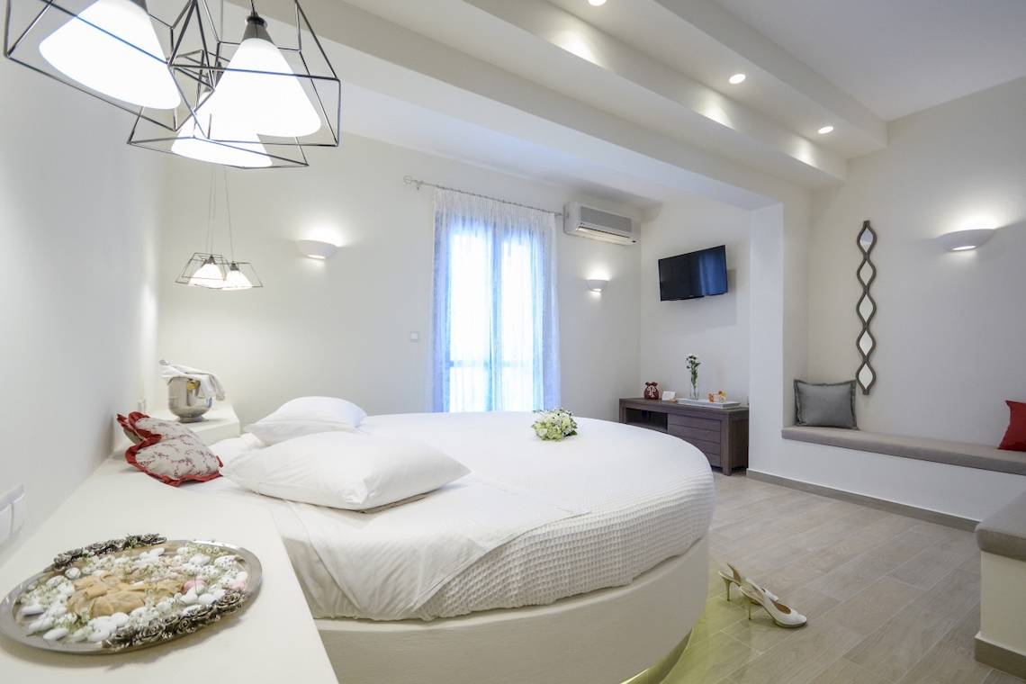 Schlafzimmer im Alkyoni Beach Hotel mit rundem Bett, weißen Kissen und Dekor.