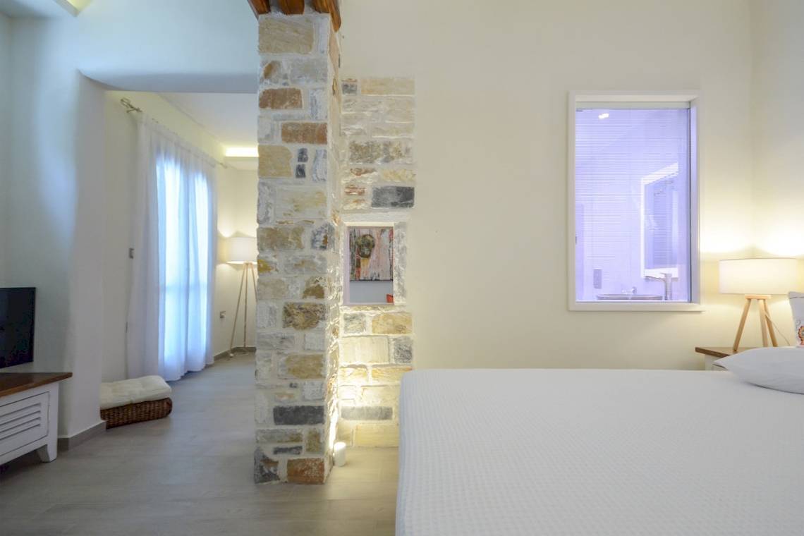 Schlafzimmer im Alkyoni Beach Hotel mit Bett, Fernseher und Steinwand.