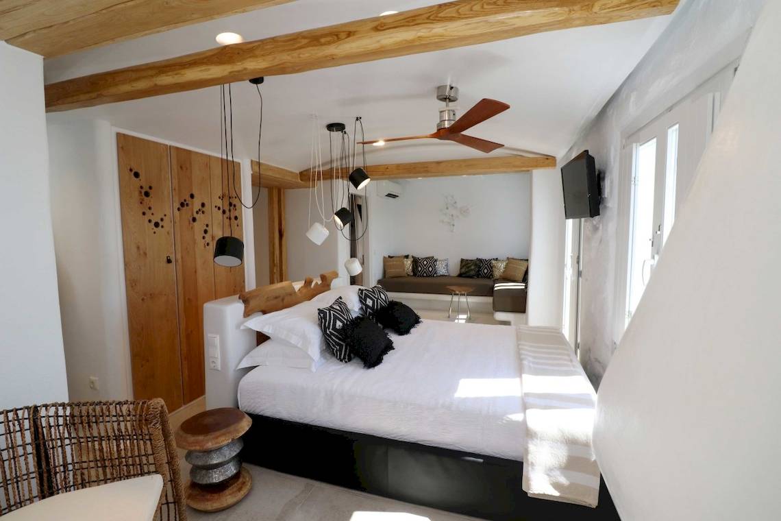 Schlafzimmer im Alkyoni Beach Hotel mit Doppelbett, weißen Wänden und Holzbalkendecke.