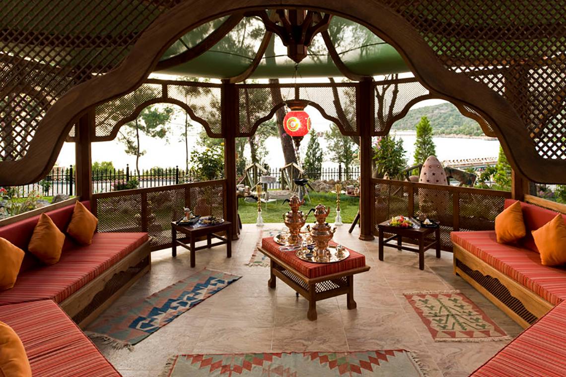 Gartenlounge im Rixos Premium Bodrum mit rotem Teppich, Sitzbank und orientalischen Lampen.