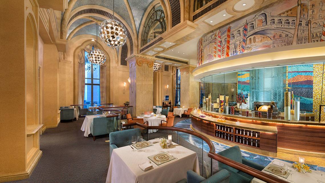 Innenansicht des Restaurants im Emirates Palace Mandarin Oriental mit runden Tischen, Kronleuchtern und einer thematischen Wand.