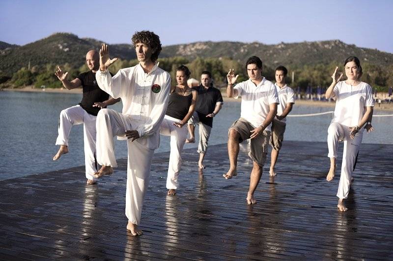 Gruppe von Menschen, die Yoga auf einem Steg am Wasser am Park Hotel Cala di Lepre machen.