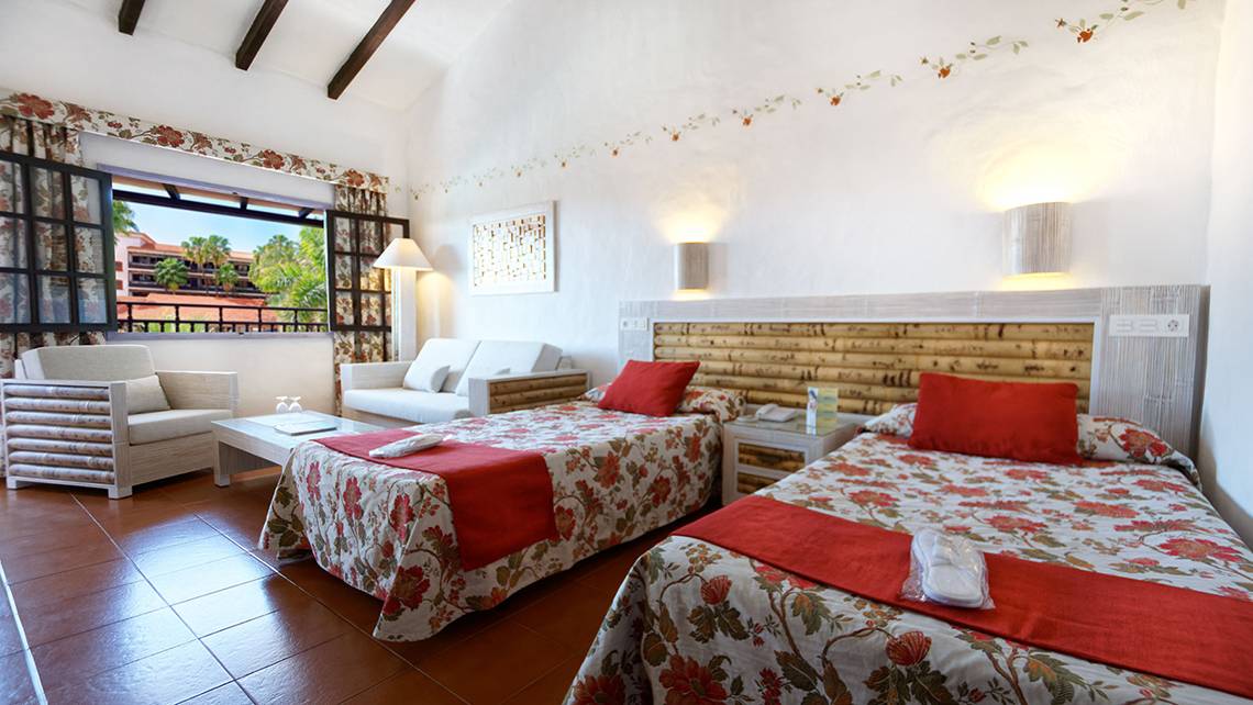 Doppelzimmer im Parque Tropical Hotel mit zwei Betten, roten Kissen und einem Wohnzimmerbereich.