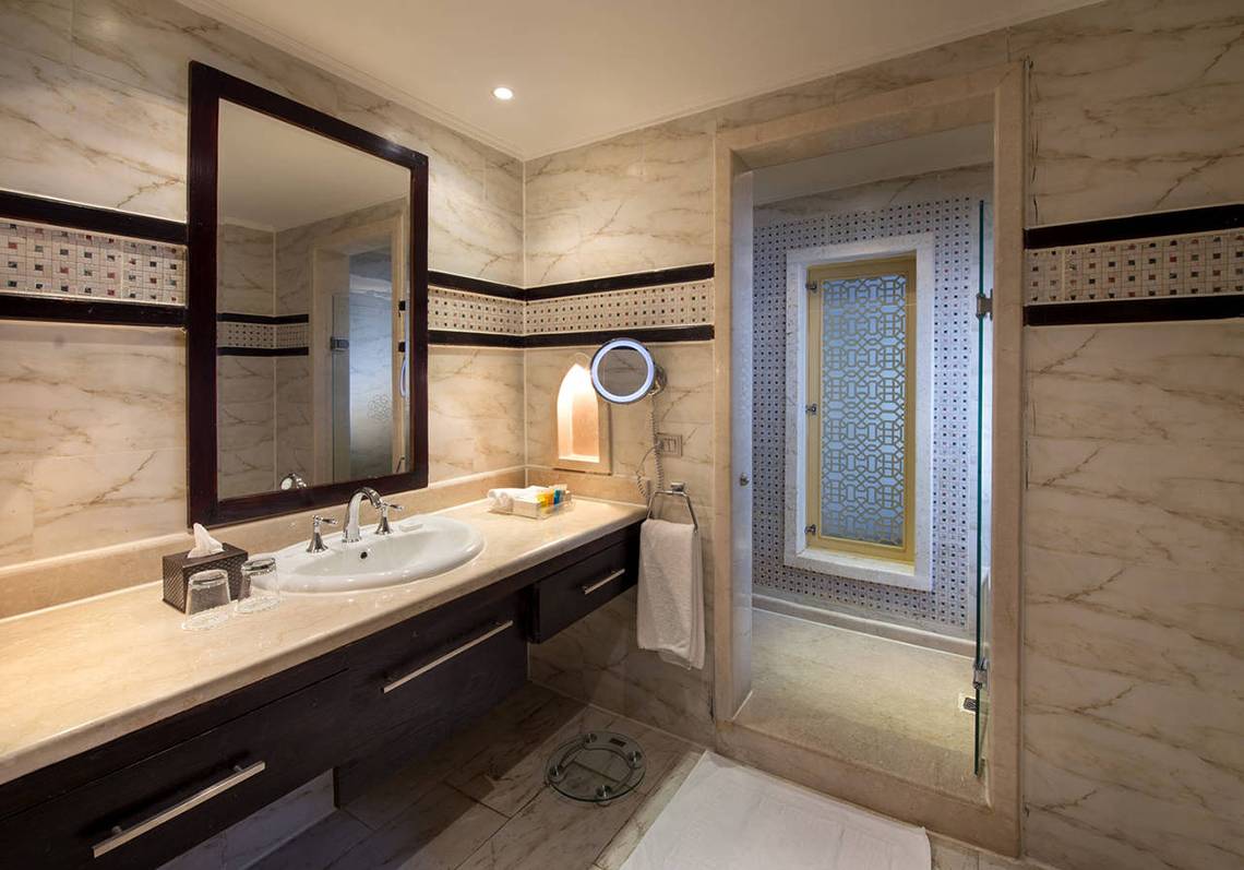 Badezimmer mit Marmorwänden, großer Spiegel und Glasdusche.