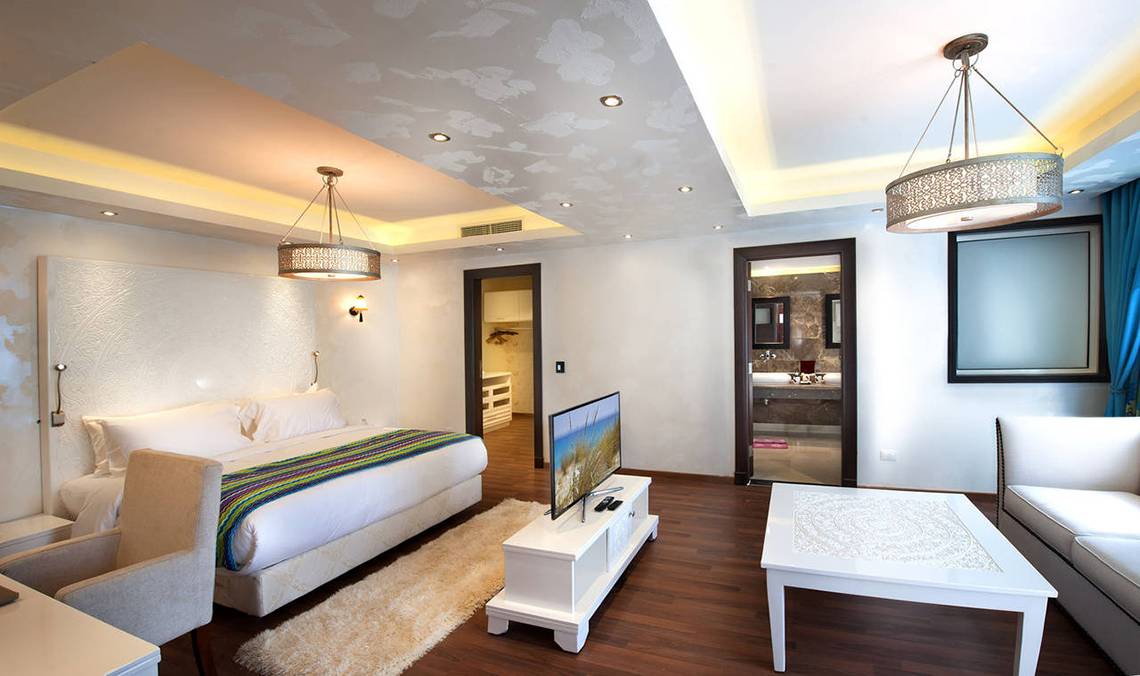 Hotelzimmer im Sunrise Arabian Beach Resort mit großem Bett, Fernseher, Tisch, Couch und modernen Möbeln.