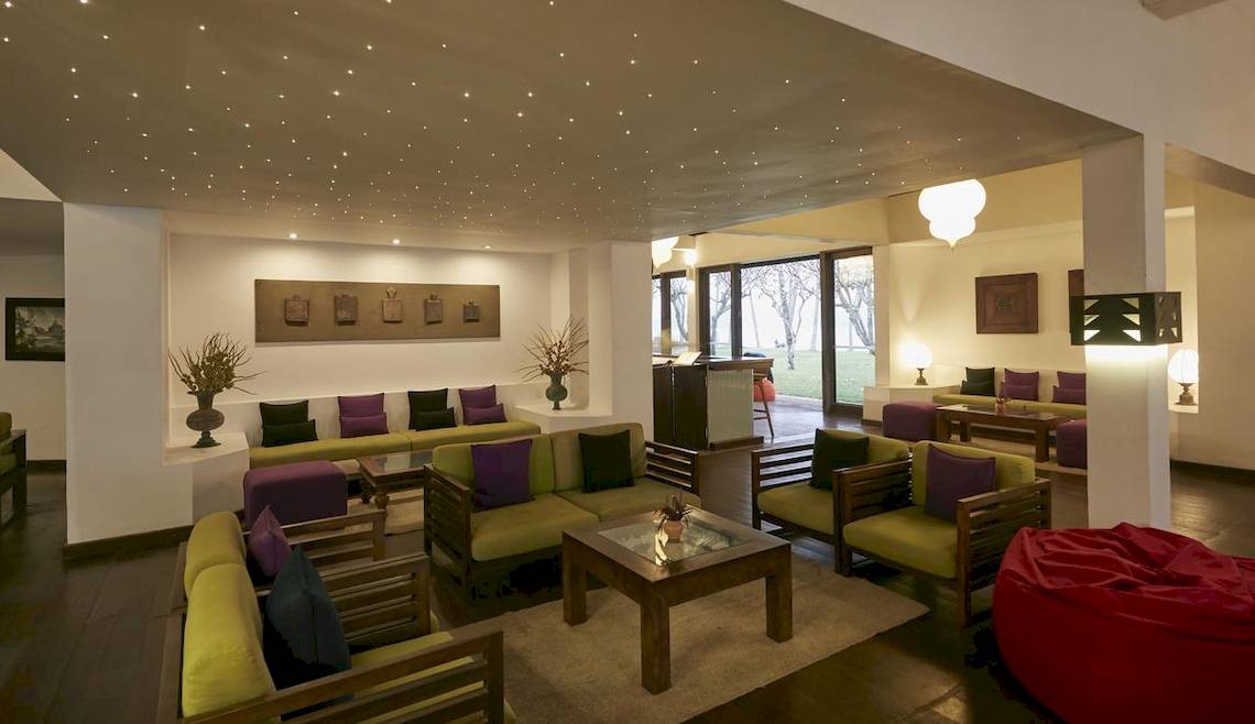 Hotellobby-Lounge des Avani Kalutara Resorts mit grünen und lila Sofas, Tischen und einem roten Pouf.