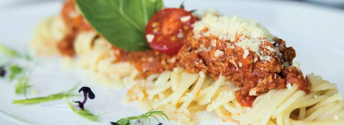 Gewürzte Spaghetti mit Fleischsoße und Käse auf einem weißen Teller serviert