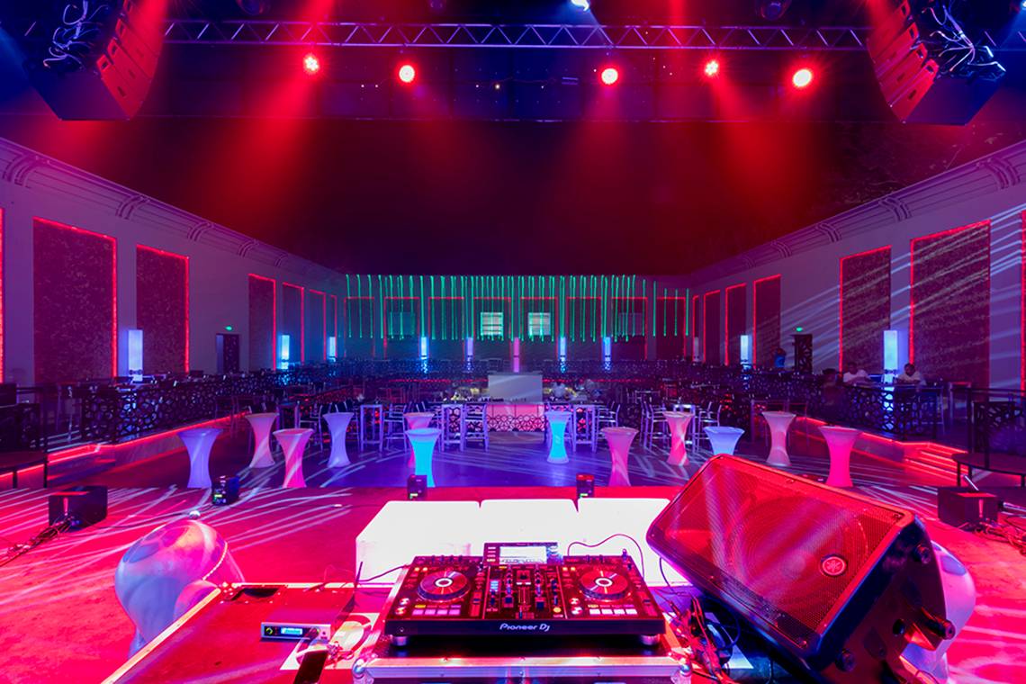Ein Veranstaltungssaal im Swandor Hotels & Resorts Topkapi Palace mit roter Beleuchtung, DJ-Anlage und weißen Tischen.