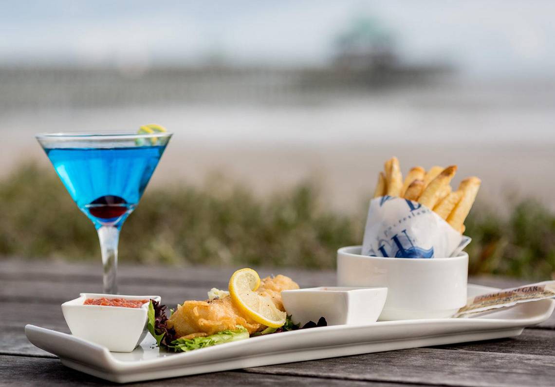 Cocktail, Fisch und Chips auf einem weißen Teller am Strand.