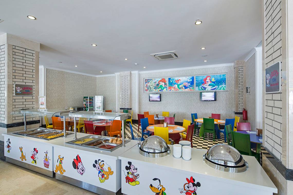 Restaurant im Crystal Waterworld Aqua Collection Hotel mit bunten Stühlen und Tischen, Fernsehern an der Wand und Essensausgabe mit Disney-Figuren.