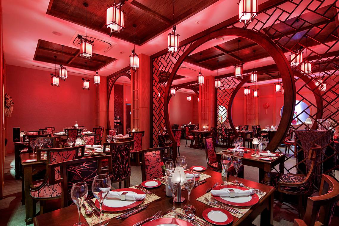 Innenansicht des Restaurants im Crystal Waterworld Resort & Spa mit roten Beleuchtung und dekorierten Tischen.