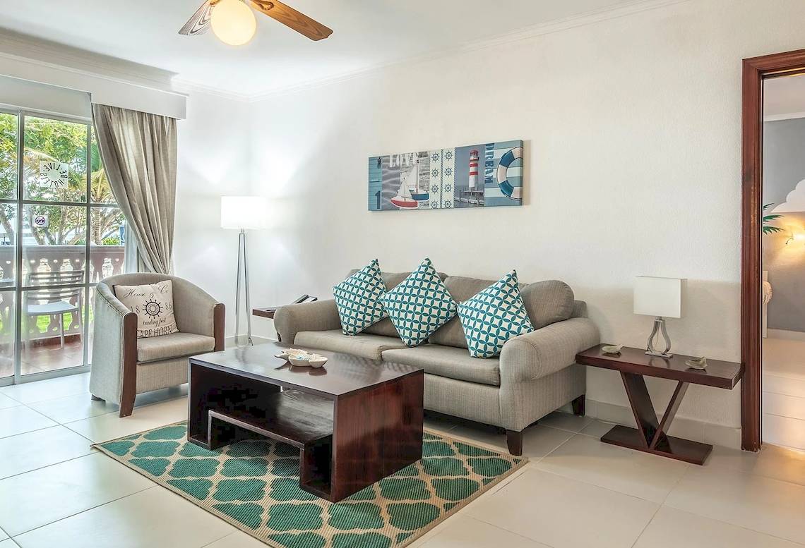 Wohnzimmer des Marien Puerto Plata Hotels mit grauem Sofa, Tisch und Dekor.