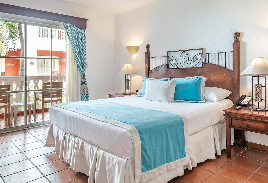 Schlafzimmer im Marien Puerto Plata Hotel mit einem Bett, Kissen, Tischlampen und einem Telefon auf einem Nachttisch.