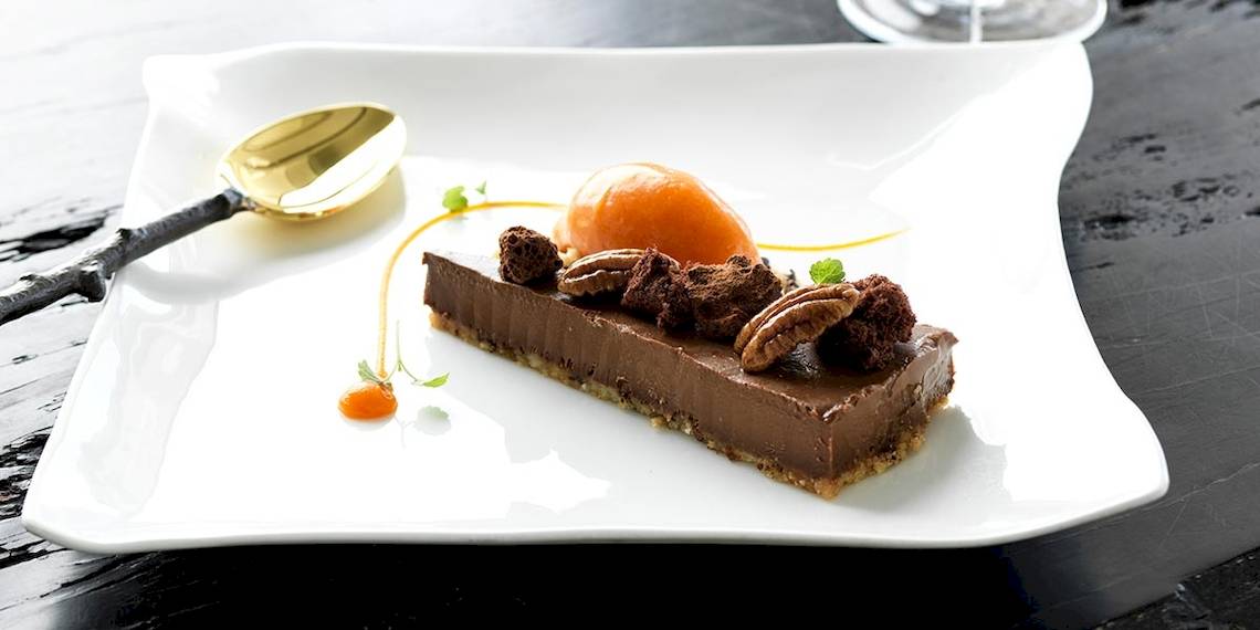 Schokoladen Tarte auf einem weißen Teller mit einem goldenen Spatel.