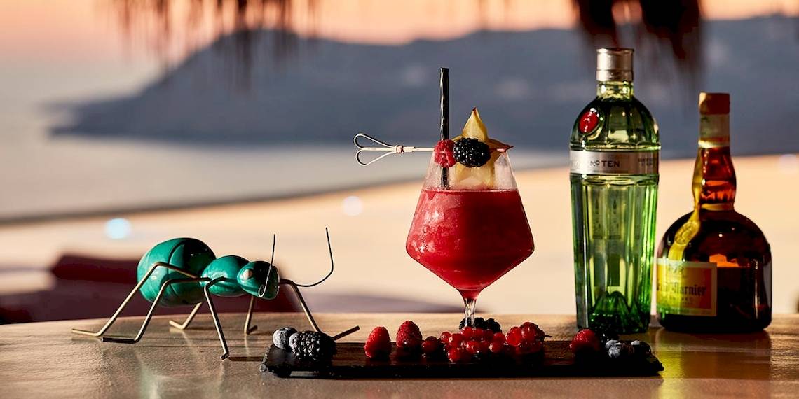 Cocktail auf einem Tisch mit einer Ameisenskulptur, Gin und anderen Getränken im Hintergrund.