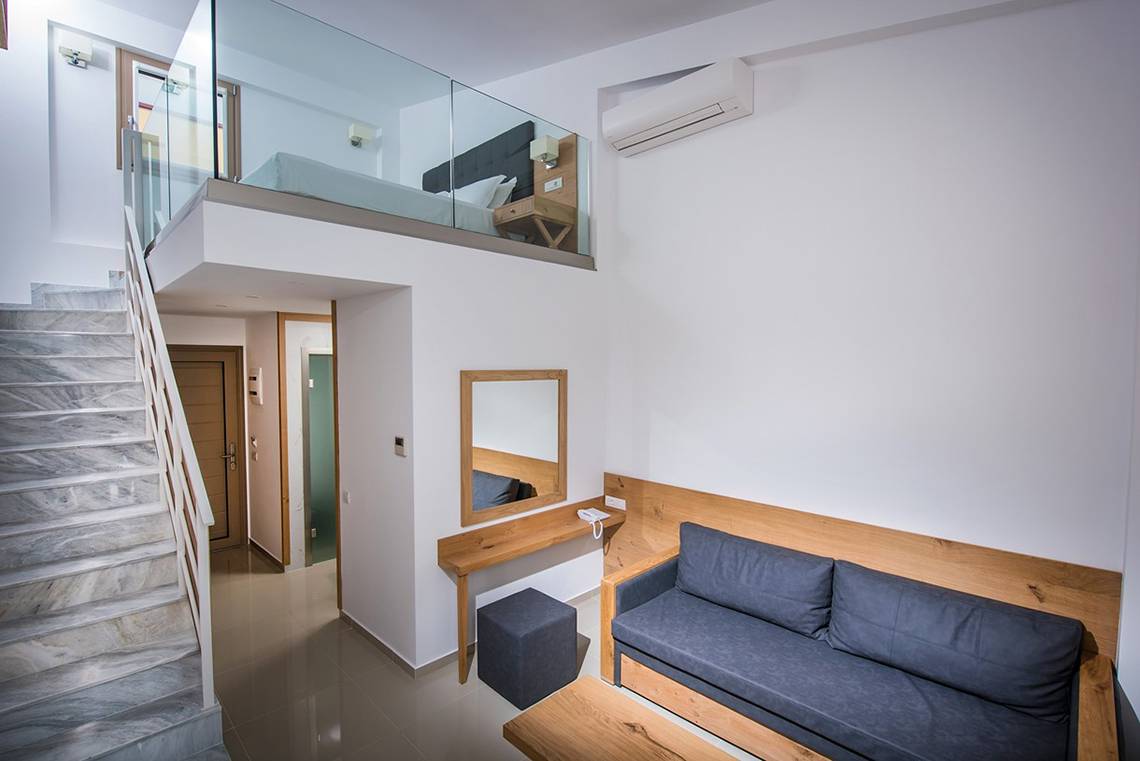 Innenbereich des Gouves Water Park Holiday Resort mit gefliester Treppe, Glasbalkon und einem Bett im oberen Stockwerk.