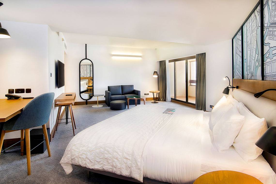 Innenansicht eines Hotelzimmers im Le Meridien Abu Dhabi mit Bett, Schreibtisch und Sofa.