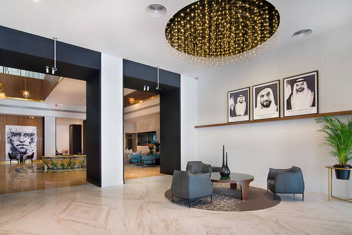 Empfangshalle des Le Meridien Abu Dhabi Hotels mit modernem Design, großen Kronleuchtern und Kunstwerken an der Wand.