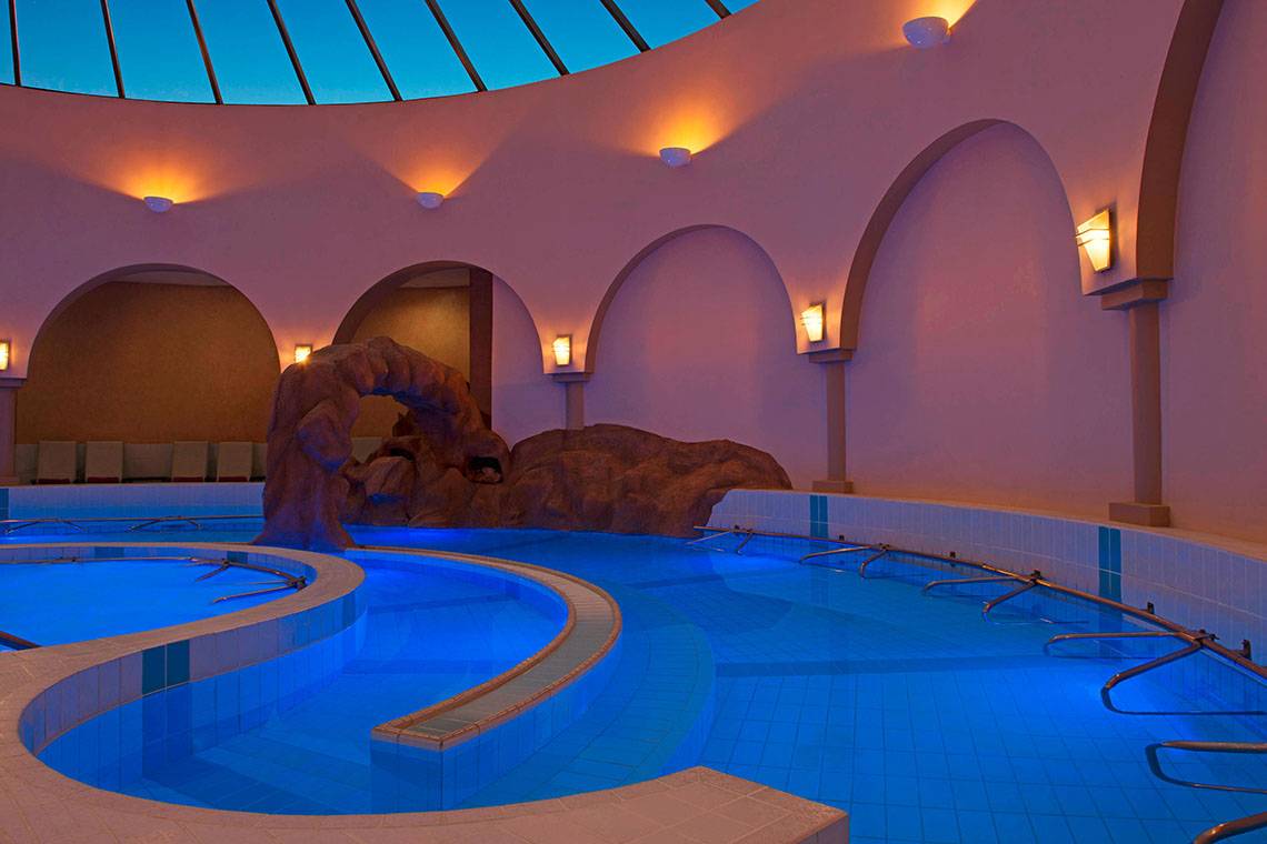 Innenansicht des Schwimmbeckens im Le Meridien Abu Dhabi mit blauen Lichtern und geformter Felsenstruktur.
