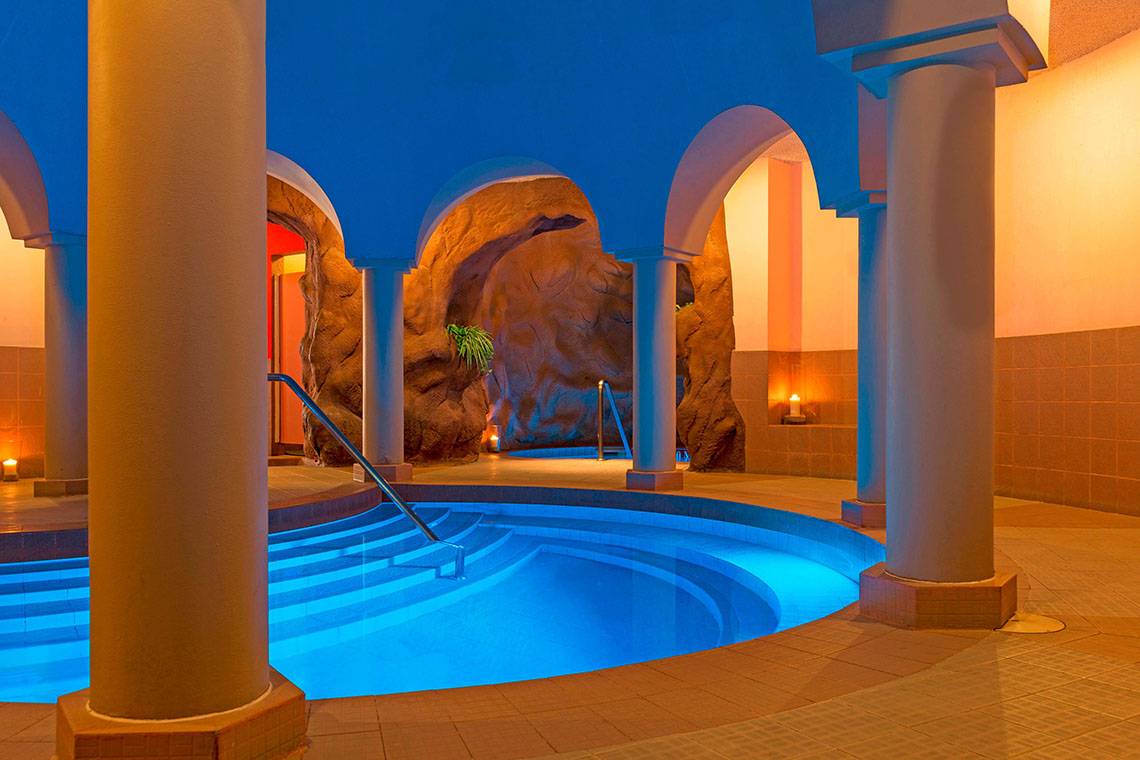 Innenpool im Le Meridien Abu Dhabi Hotel mit blau beleuchtetem Wasser und Säulen.
